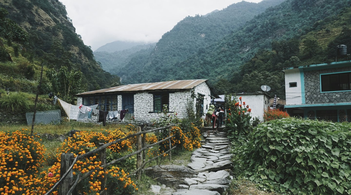 Stone‑walled Himalayan tea house with outdoor tables and tent against misty mountain slopes