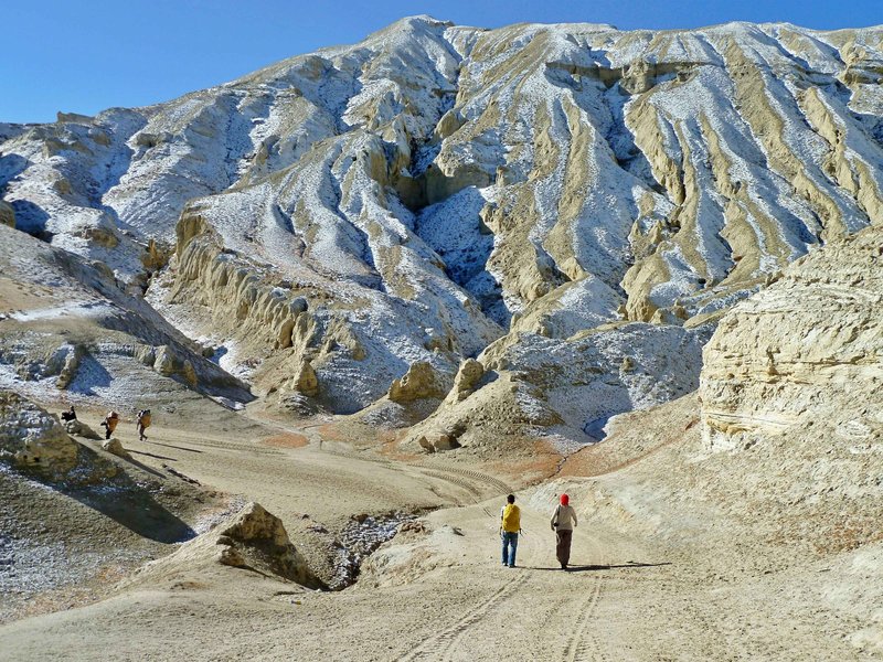 Trekkers walking through the rugged Himalayan desert landscape of Upper Mustang, Nepal during a motorbike tour