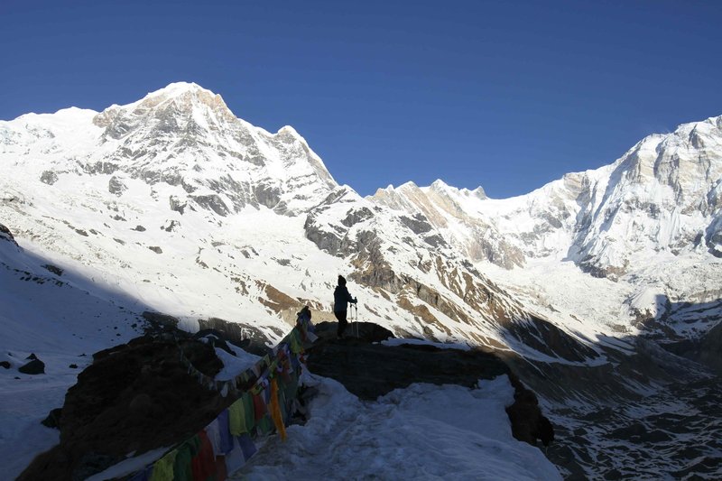 Panoramic view of snow-covered Himalayan peaks from Pikey Peak trek in Nepal with colorful prayer flags under clear blue sky.