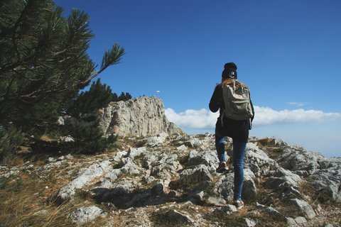 “Woman trekking along a rocky talus path of Manaslu region with snow-capped peaks rising in the distance.”