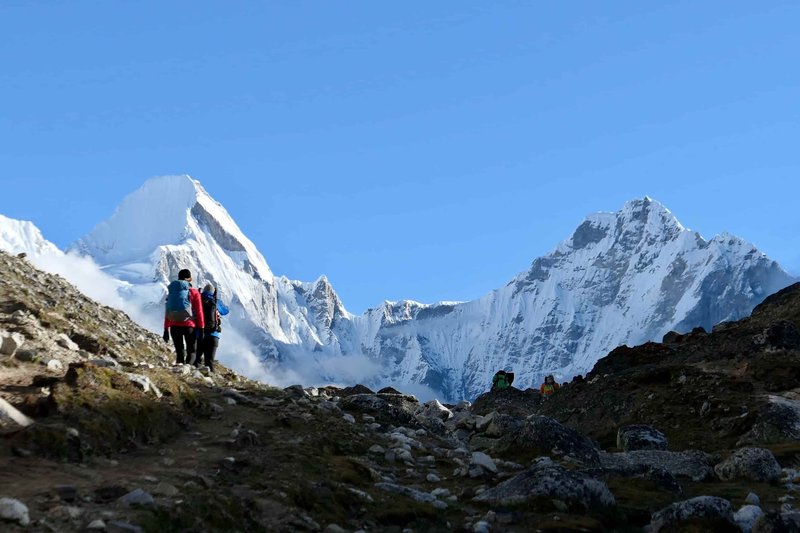 Group of trekkers hiking along rocky trail towards snow-capped mountains on the Pikey Peak trek, Nepal Himalayas.