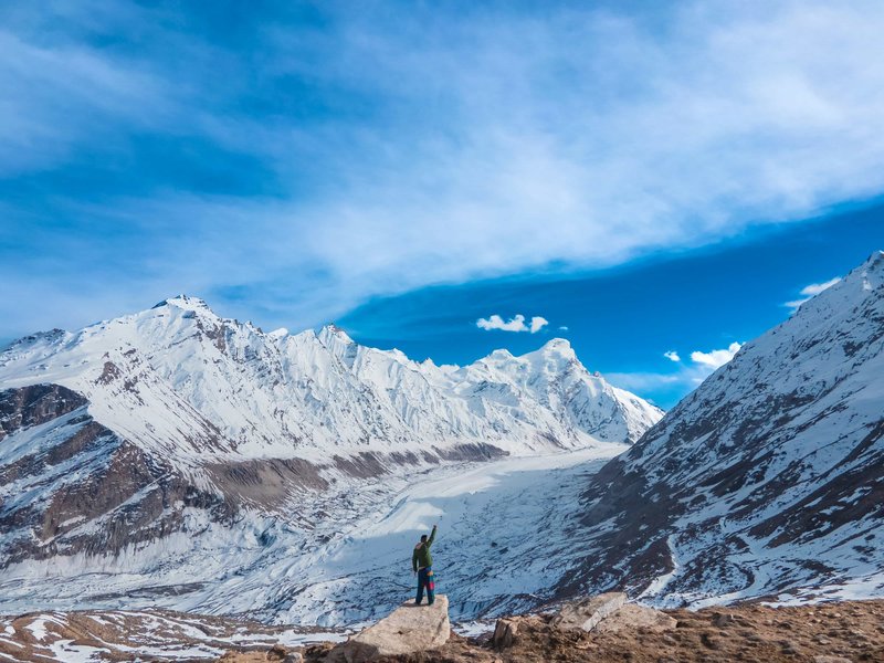 Solo trekker standing on rock overlooking Annapurna glacier valley with snow-covered Himalayan peaks and dramatic clouds on ABC trek Nepal
