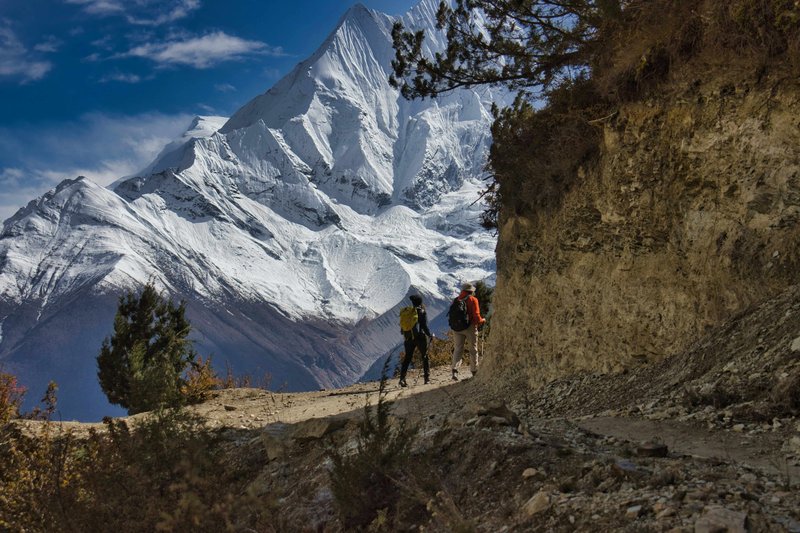 Two trekkers hiking narrow mountain trail with iconic Machapuchare Fishtail Mountain backdrop on Annapurna Base Camp trek route